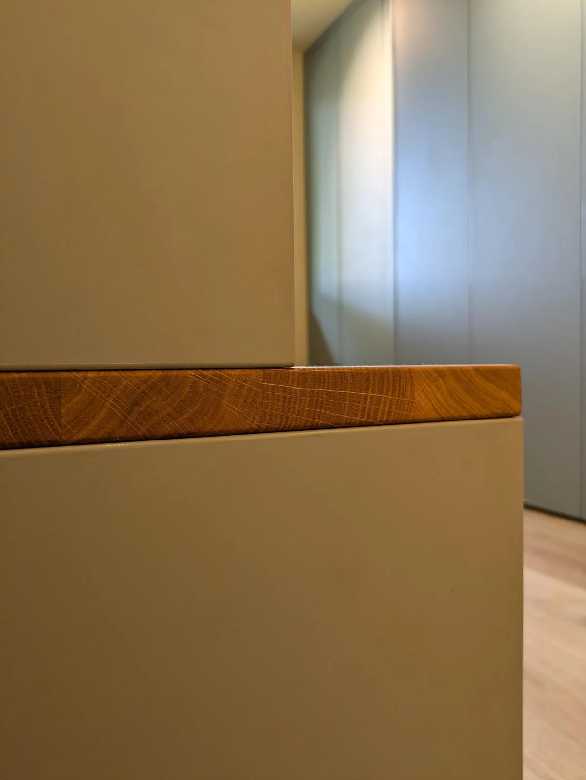 Nahaufnahme einer warmen Holzkante mit sichtbarer Maserung zwischen taupefarbenen Möbelflächen