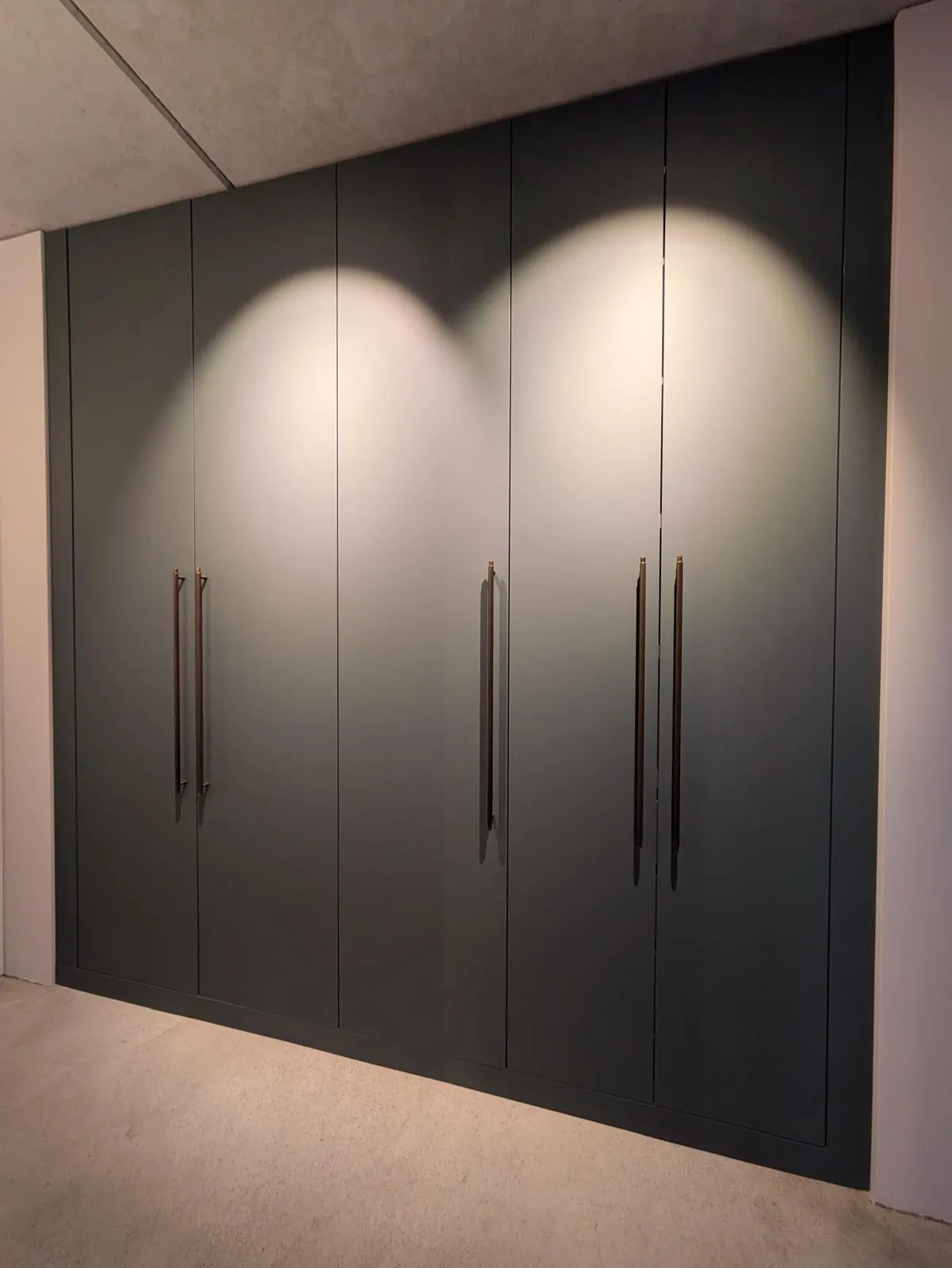 Ein raumhoher Schrank mit dunklen Fronten und langen, schlanken Griffen.