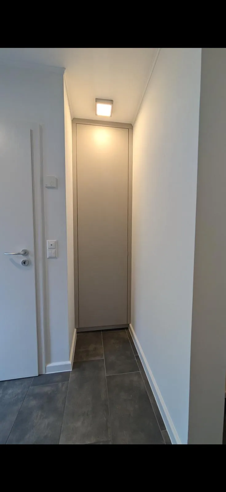 Ein schmaler, hoher Schrank füllt die Nische am Ende eines Flurs mit einer geschlossenen Front.