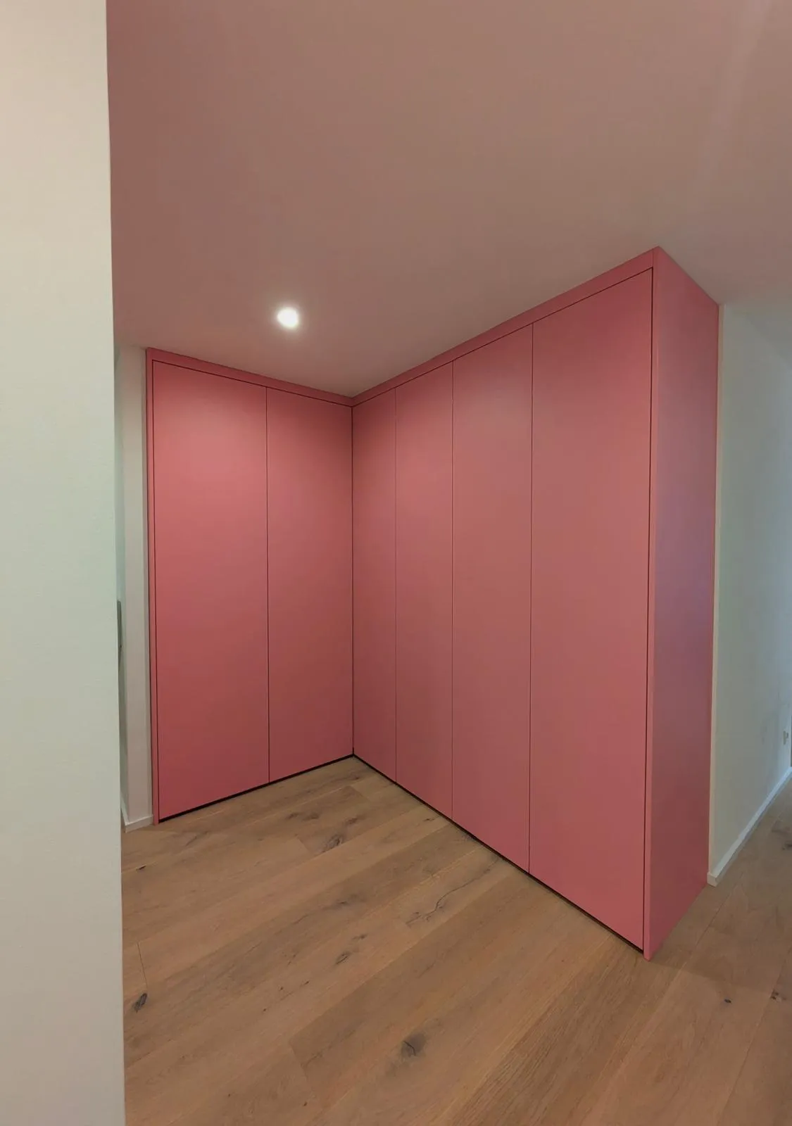 Ein rosafarbener Einbauschrank nutzt die Ecke des Raumes und setzt einen sanften Farbakzent.
