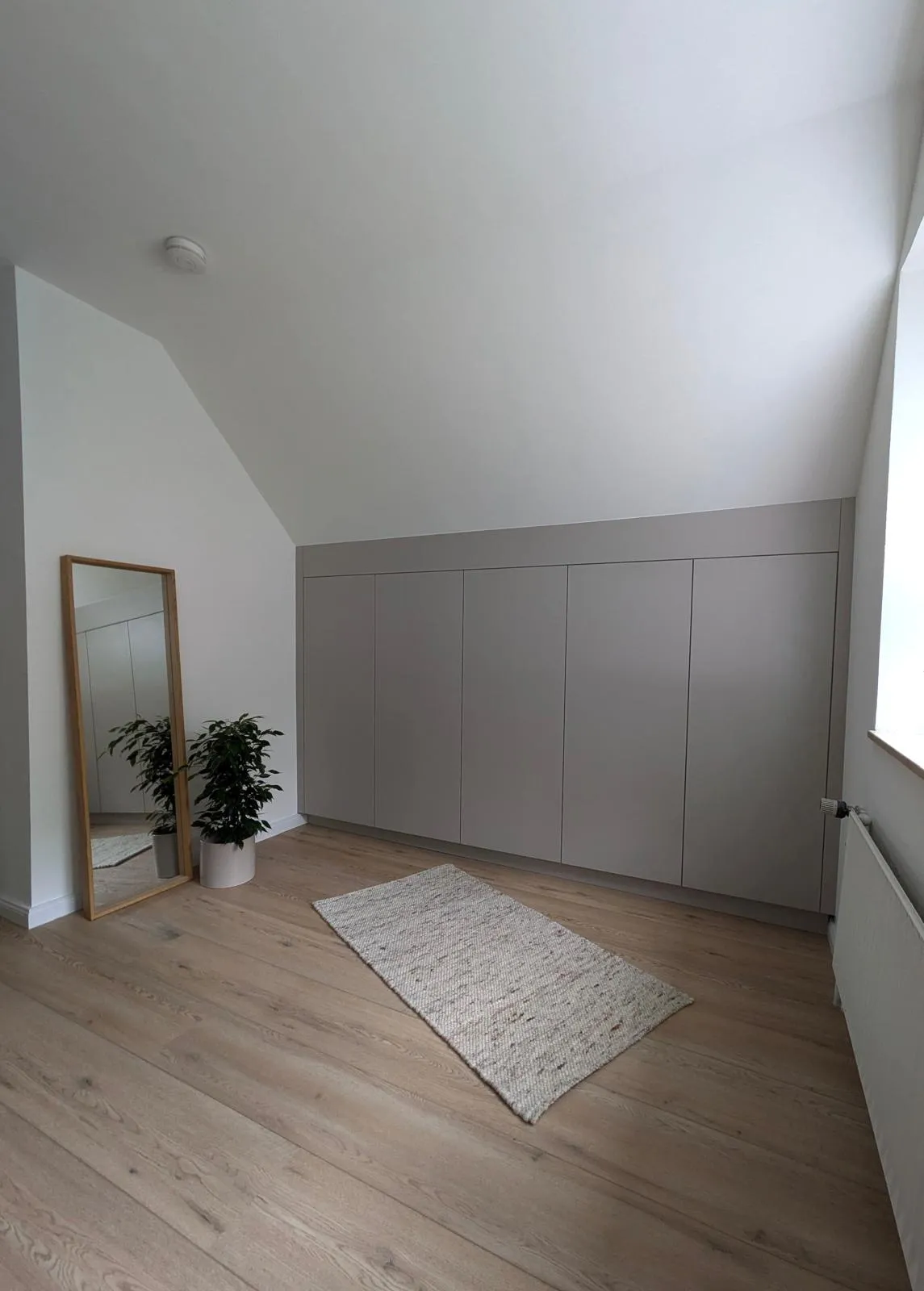 Eine ruhige, geschlossene Schrankfront folgt der Dachschräge. Der Raum bleibt offen und bietet Platz zum Ankommen.