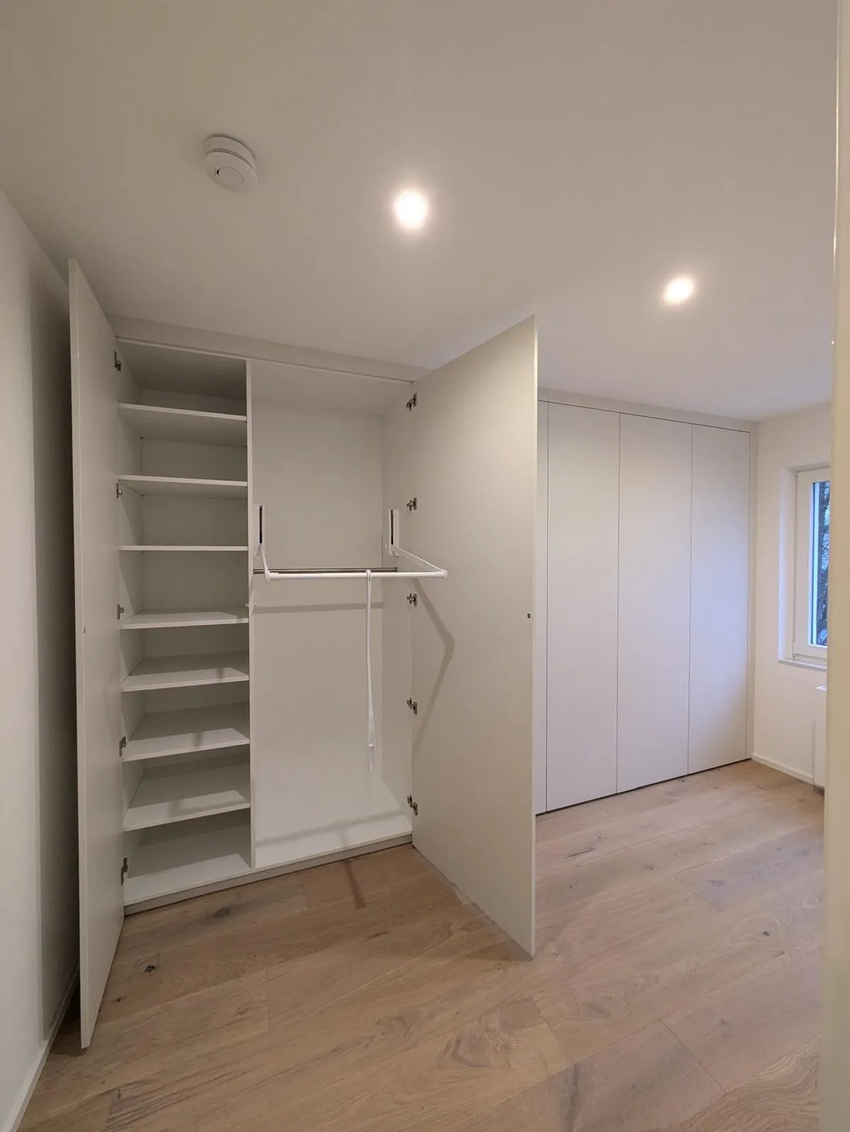 Geöffneter weißer Einbauschrank mit Regalfächern und einem heruntergezogenen Garderobenlift